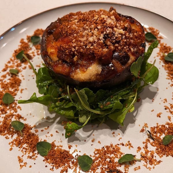 Stuffed mushroom with melted cheese and breadcrumbs, served on a bed of arugula with herb garnish.