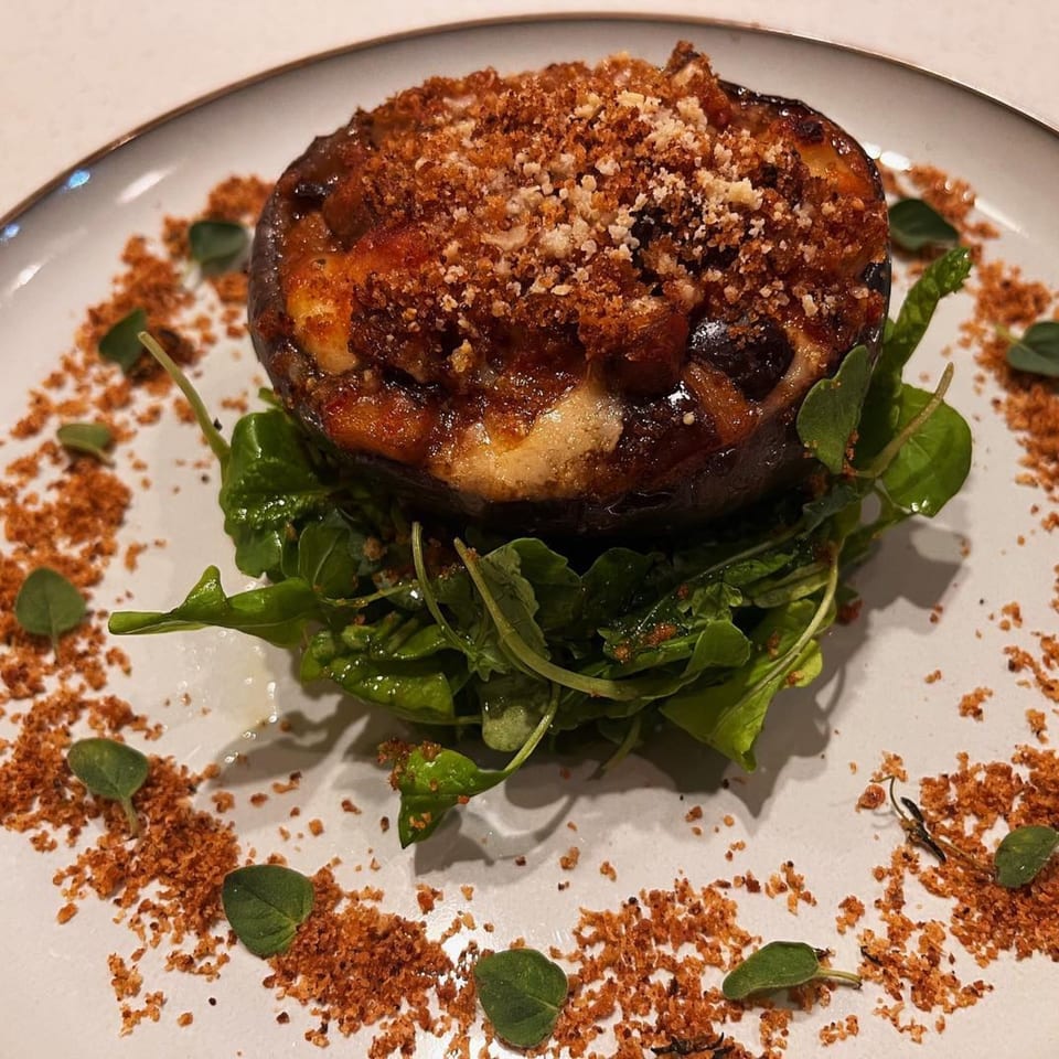 Stuffed mushroom with melted cheese and breadcrumbs, served on a bed of arugula with herb garnish.