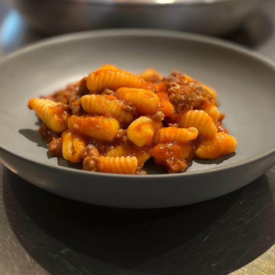 A dark gray bowl filled with gnocchi and a rich red meat sauce, ready to be served.