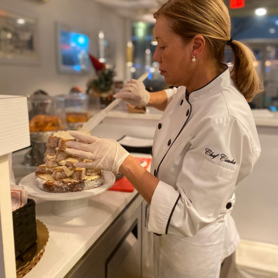 Chef Claudia in a white chef's coat and gloves, assembling a dessert on a white cake stand.