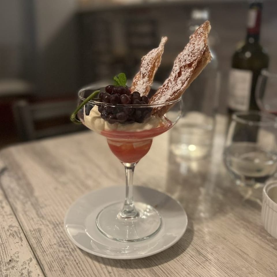 Italian dessert in a martini glass with grapes, cream, and two powdered sugar pastries.
