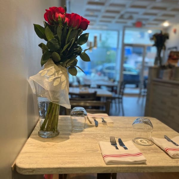 A vase of red roses on a set table with cutlery and glasses in an Italian restaurant.