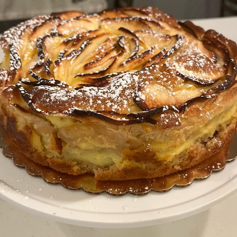 A golden-brown apple tart with powdered sugar, featuring fanned apple slices and creamy filling.