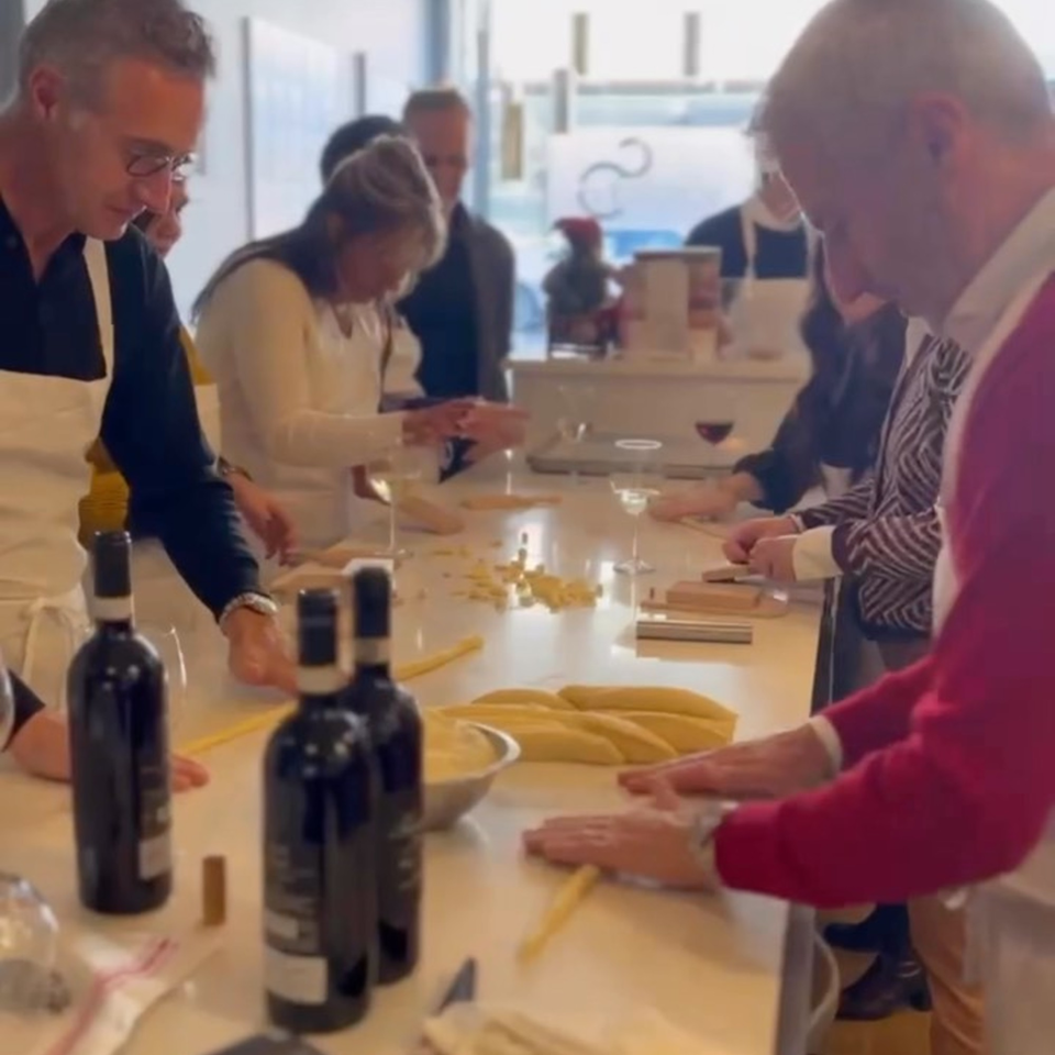 People in aprons making fresh pasta by hand at a cooking class with wine bottles on the table.